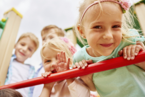 Charming little girl leaning on jungle gym ladder surrounded by her friends