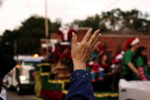 A person waves toward holiday parade floats and participants during a Christmas celebration.